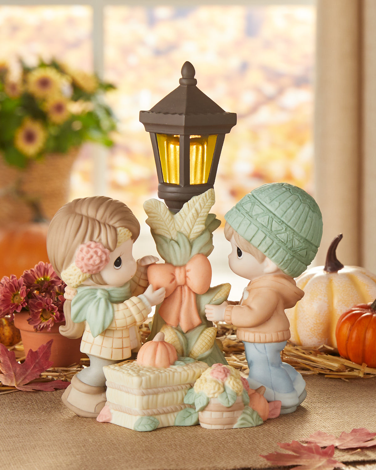 Two figurines by a lantern with pumpkins and flowers in the background
