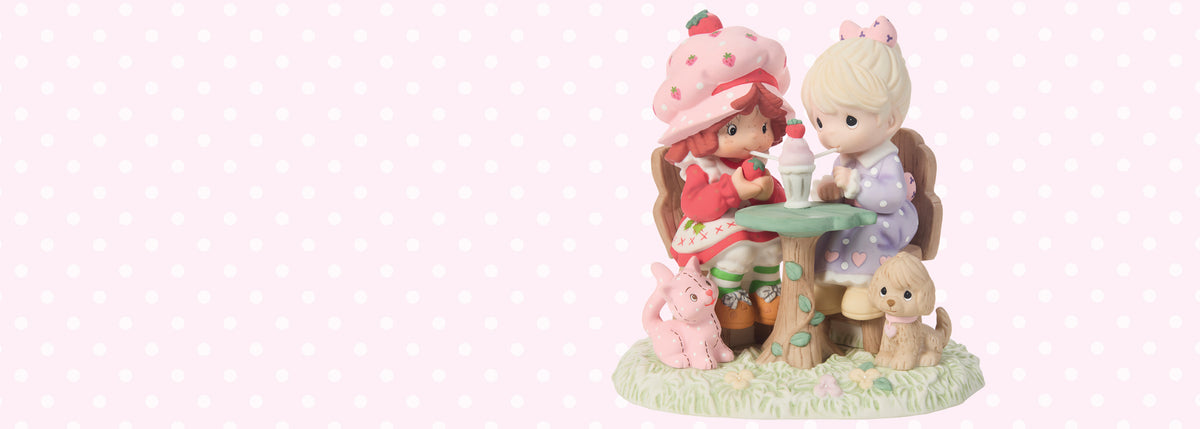 A ceramic figurine of two young girls sitting at a small table with a pink bunny and a tan dog, set against a light pink polka-dot background.