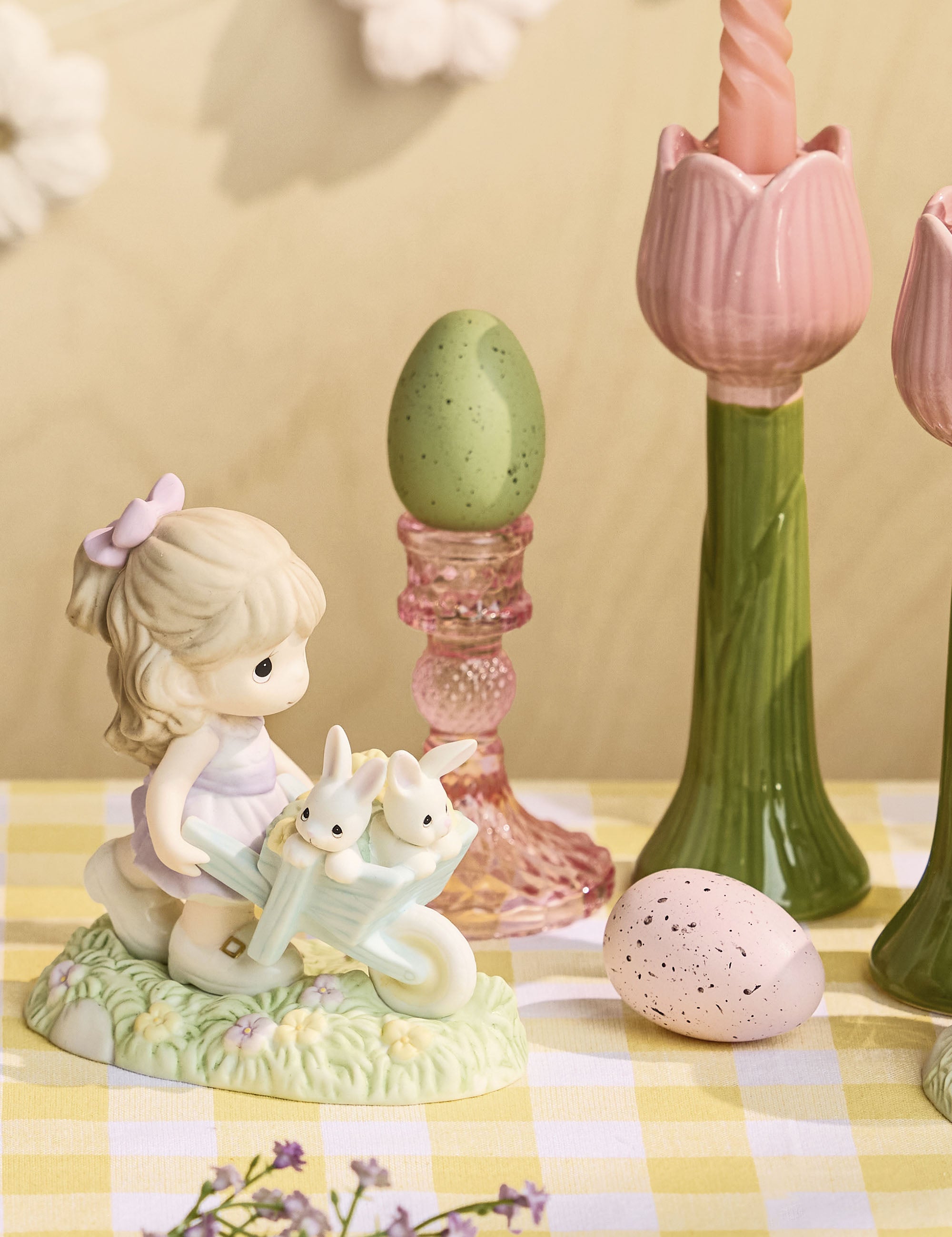Decorative scene with a figurine of a girl with a dog, Easter eggs, and candlesticks on a checkered tablecloth.